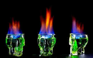 Citizens, what do you do when the legendary Mark Hamill, not just the actor behind Luke Skywalker but also the amazing voice actor behind “The Joker” deigns to like your humble Leader’s blog? YOU HONOR THE MAN, THAT’S WHAT YOU DO! ☺ Mr. Hamill, I give you an Absinthe-based cocktail to honor your incredible work as the Clown Prince of Crime – “The Joker’s Wild!” The original way of preparing Absinthe is called the French Absinthe Ritual, where the focus is set on the “Louche”, the change of Absinthe´s color when it is diluted with ice-cold water. Despite popular belief, the original Absinthe ritual does not include pouring Absinthe over sugar and then setting it on fire. This way of drinking Absinthe is called the “Fire Ritual” or the modern “Bohemian Ritual”. For the Joker’s Wild, we will combine both rituals with a unique twist. Take a skull-shaped glass, fill it ¼ with Absinthe (preferably French) as to indulge in madness locked within a skull is the Joker’s way. Take one sugar cube, and put it onto an absinthe spoon or a fork. Carefully pour 1 teaspoon of Violet syrup over the cube (as all madness must have an element of sweetness and nature’s harmony to disrupt), then pour just enough ice-cold water over the sugar cube to enable the milky “louche” effect to spread through the absinthe in a thin curl, as madness clouds the mind. Remove the spoon/fork with the sugar cube and CAREFULLY light the absinthe with a long match, and let it burn as insanity does in the mind of the Clown Prince of Crime! Blow it out after 3 seconds, return the spoon/fork/sugar and add more ice cold water gently flowing over the cube to completely cloud the absinthe and the sugar is dissolved. Float 3 teaspoons of crème de violette over the absinthe, observe the colors of the Joker, the metaphors inherent in this libation and drink to the point of losing all control. Be sure your designated driver does NOT imbibe! Thank you again, Mark Hamill, for brightening the day of an unworthy Genralissimo!